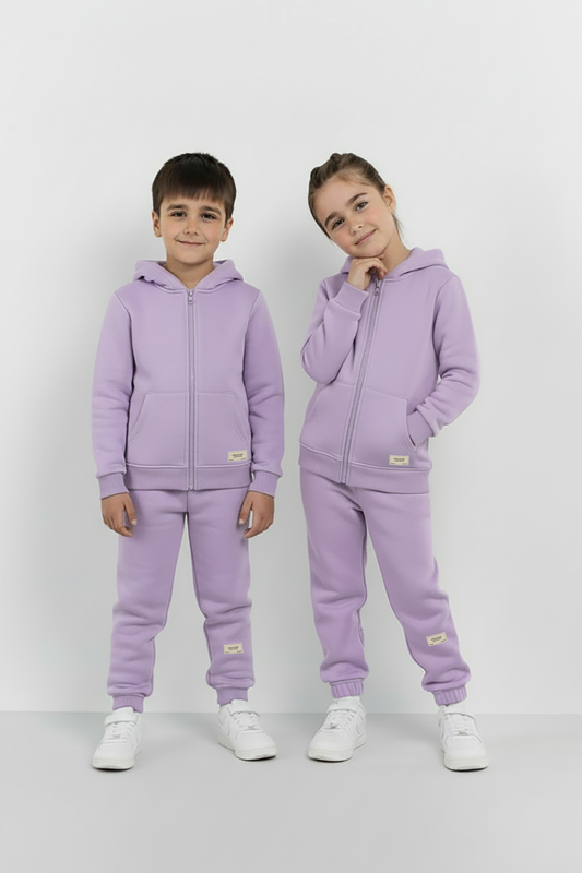 Two children wearing matching lavender tracksuits on a white background