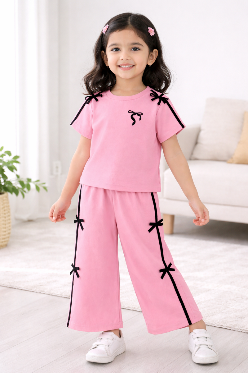 Young girl wearing a pink outfit with black bows in a room with a white couch and plant.